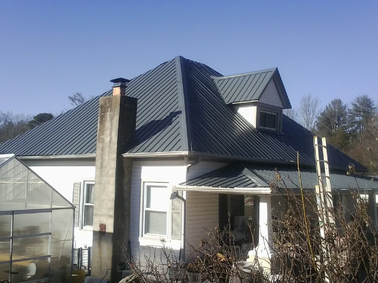 Dark blue standing seam metal roof on a white farmhouse with dormer — Slate & Tile Roof Repair by Roofing Brothers in Esmond