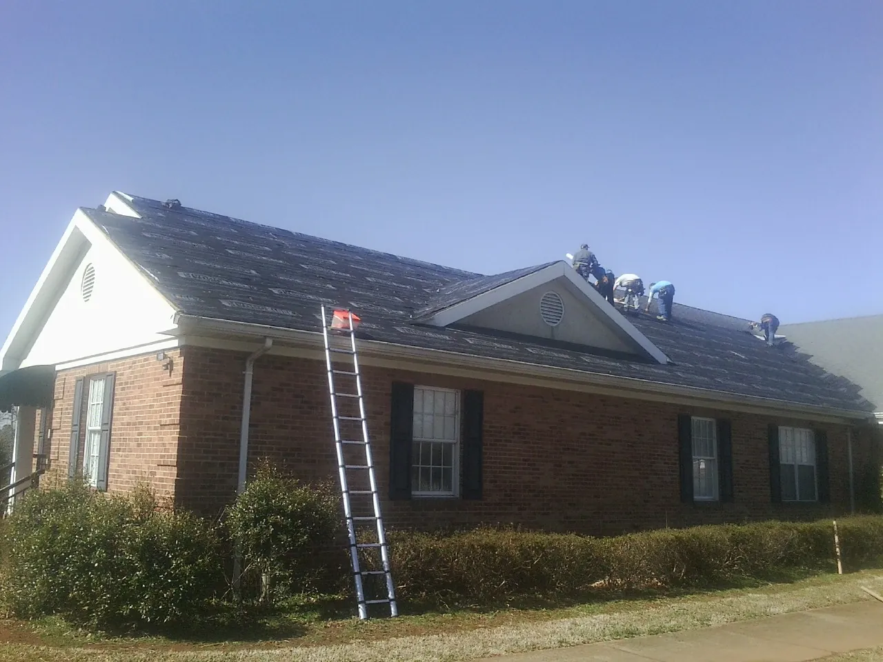Crew tearing shingles off a brick ranch roof with a ladder set — Emergency Roof Repair work by our crew in Esmond