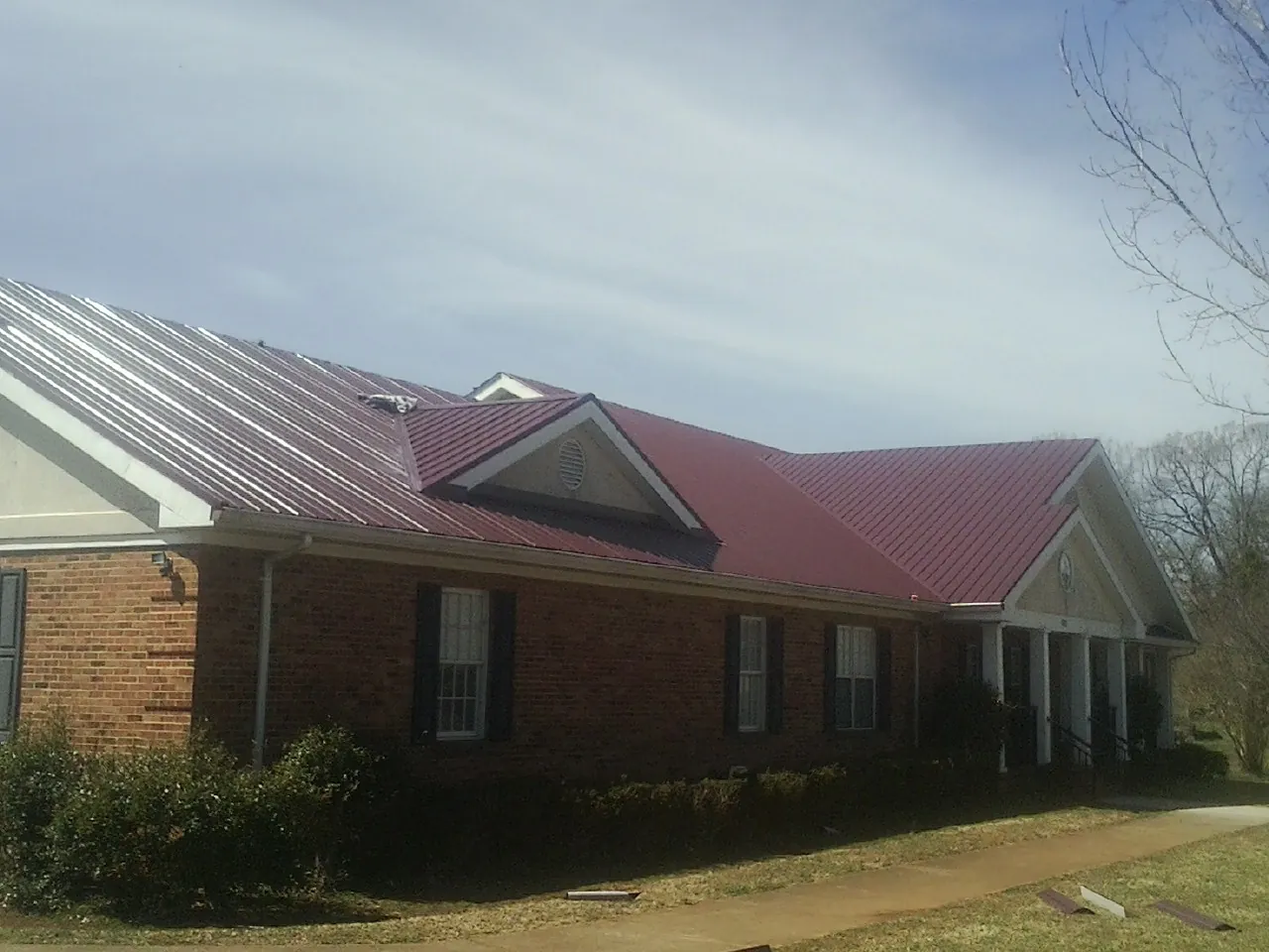 Red metal roof with gabled entries on a long brick building, from a Hail Damage Roof Repair job in Esmond