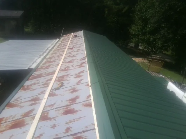 Old rusted panels beside newly installed green metal roofing — Wind Damage Roof Repair by Roofing Brothers in Esmond