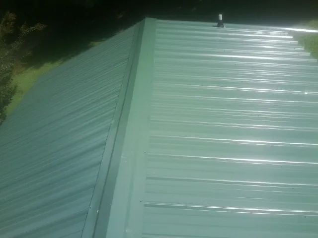 New green metal panels meeting at the ridge of a roof — Flat Roof Repair work by our crew in Esmond