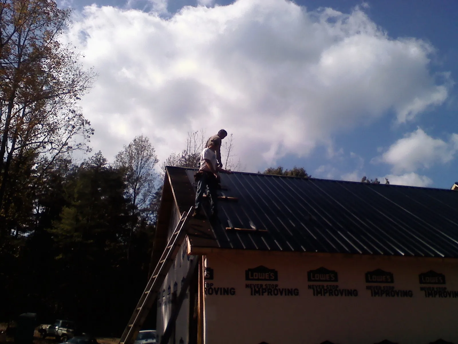 Roofer fastening dark metal panels high against a cloudy sky, from a Roof Inspection job in Esmond