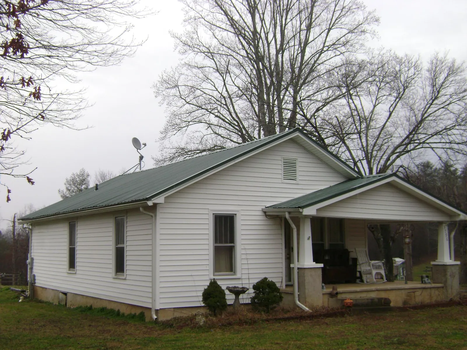 Green metal roof on a white bungalow with a side porch in Esmond