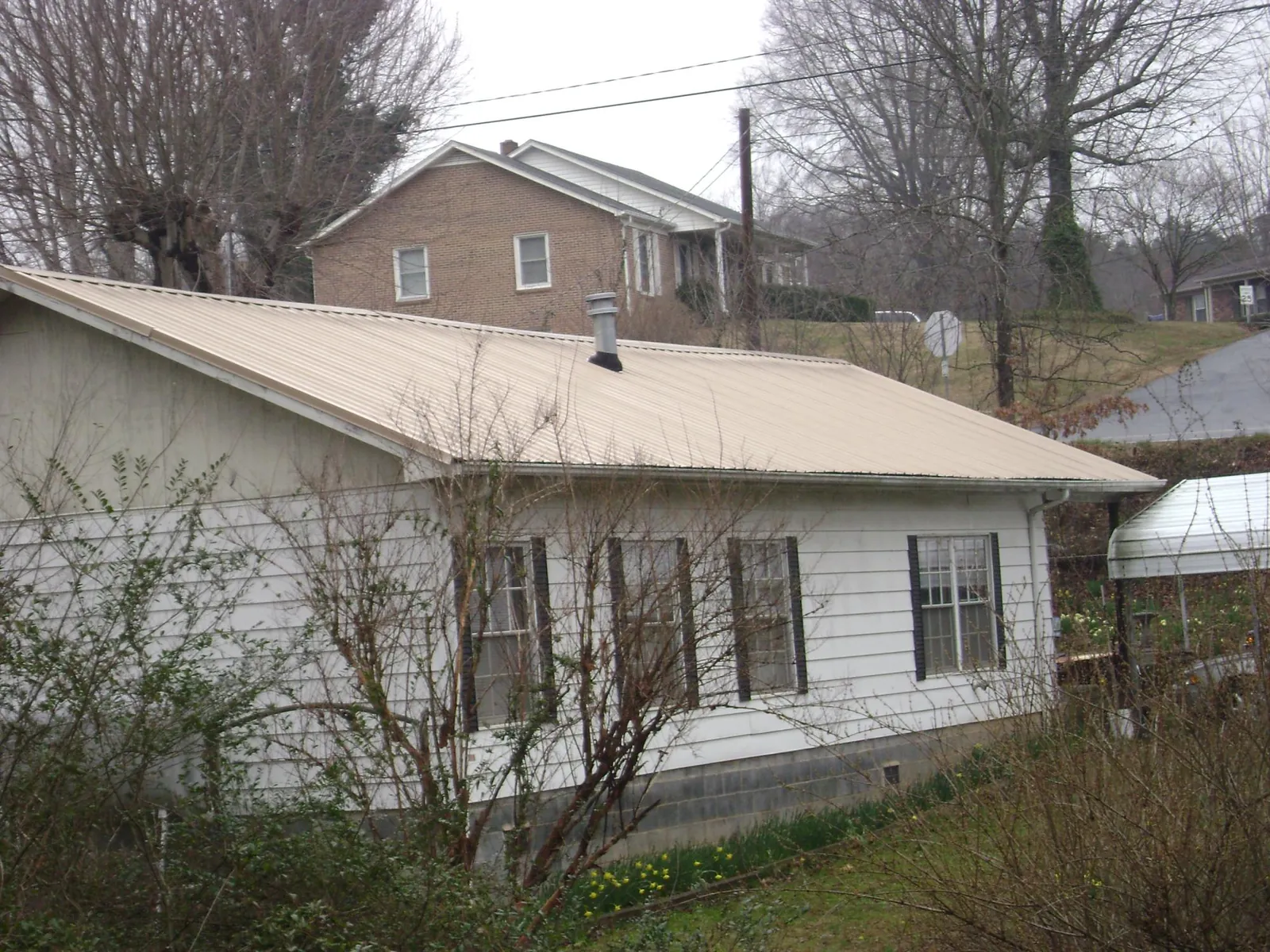 Tan metal roof on a white sided house set into a hillside — Commercial Roofing by Roofing Brothers in Esmond