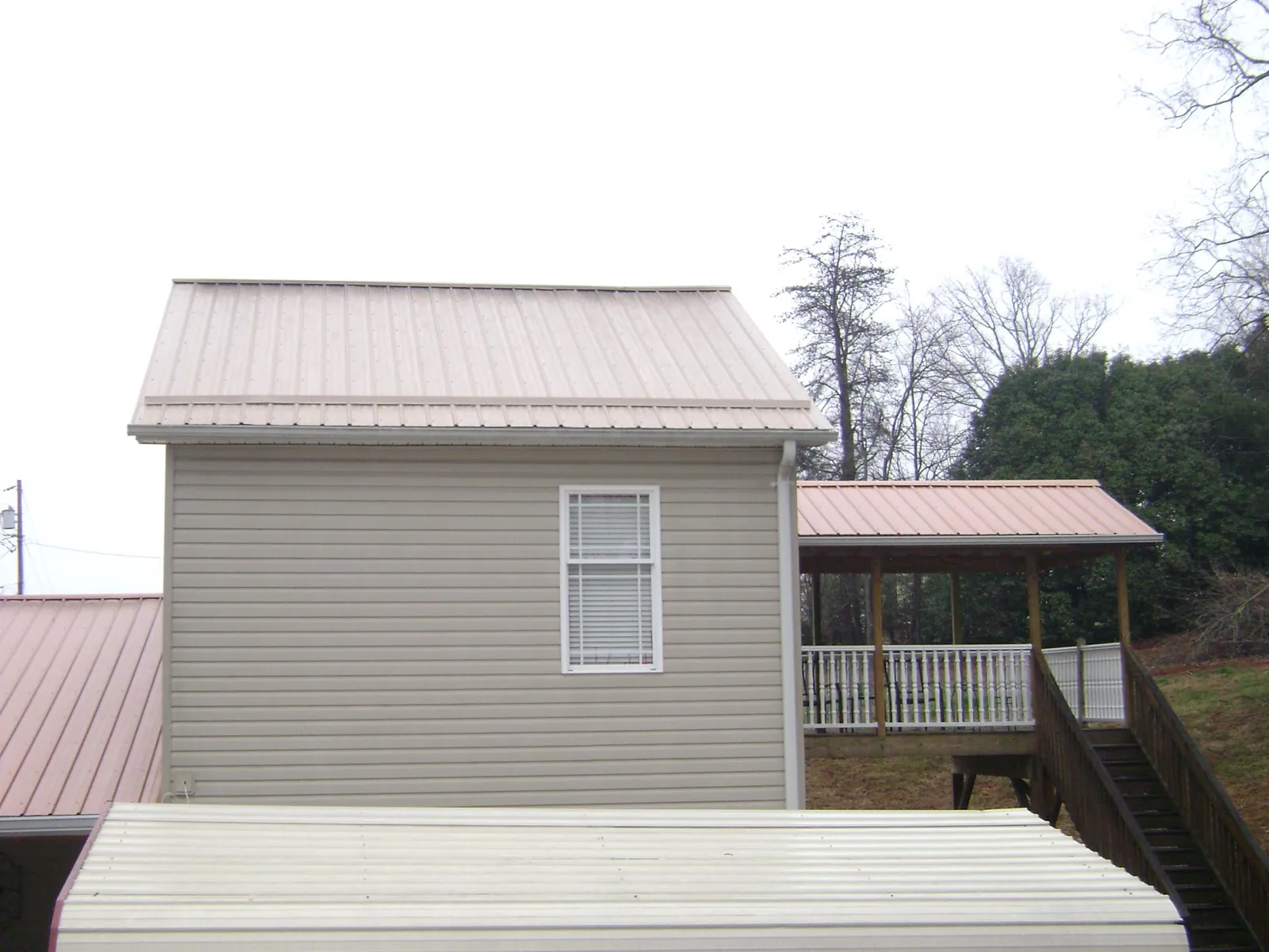 Tan metal roofs on a two story addition and attached porch, from a Roof Replacement job in Esmond